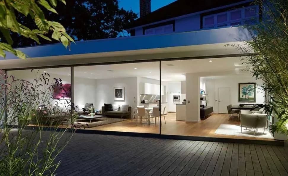 Wide slim sliding glass door opening a modern living room onto a garden at night