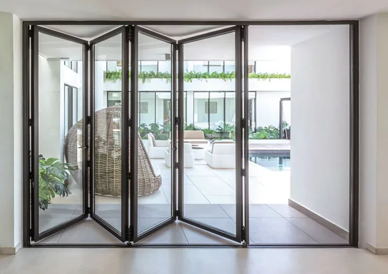 Slim black aluminium bi-folding door panels folded in pairs, viewed from inside towards a courtyard